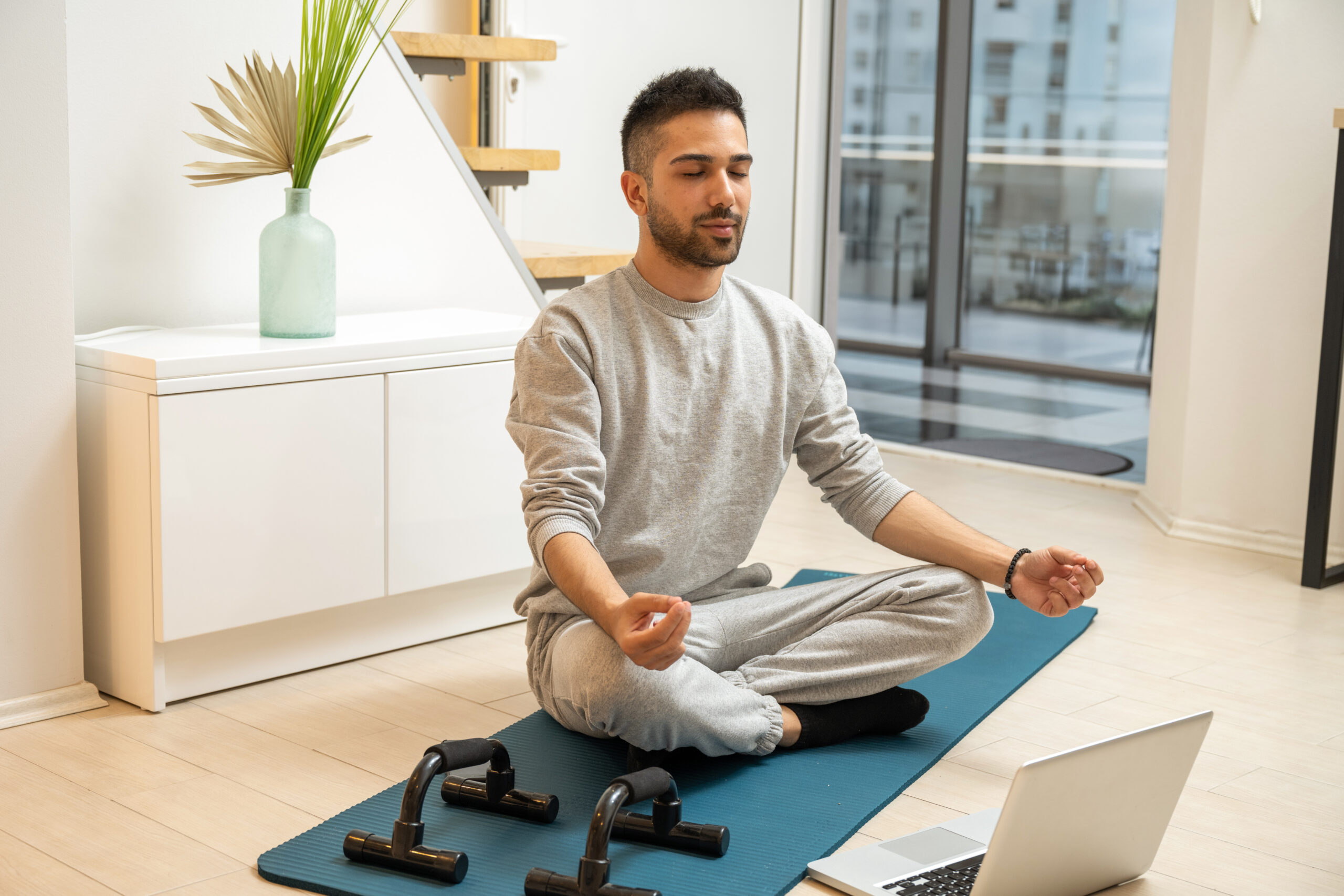 Man meditating on a yoga mat with a laptop nearby